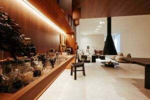 Detalhe do bar em marcenaria com garrafas e taças, com vista para o living e lareira suspensa do ambiente ATO_26, CasaCor RS 2026